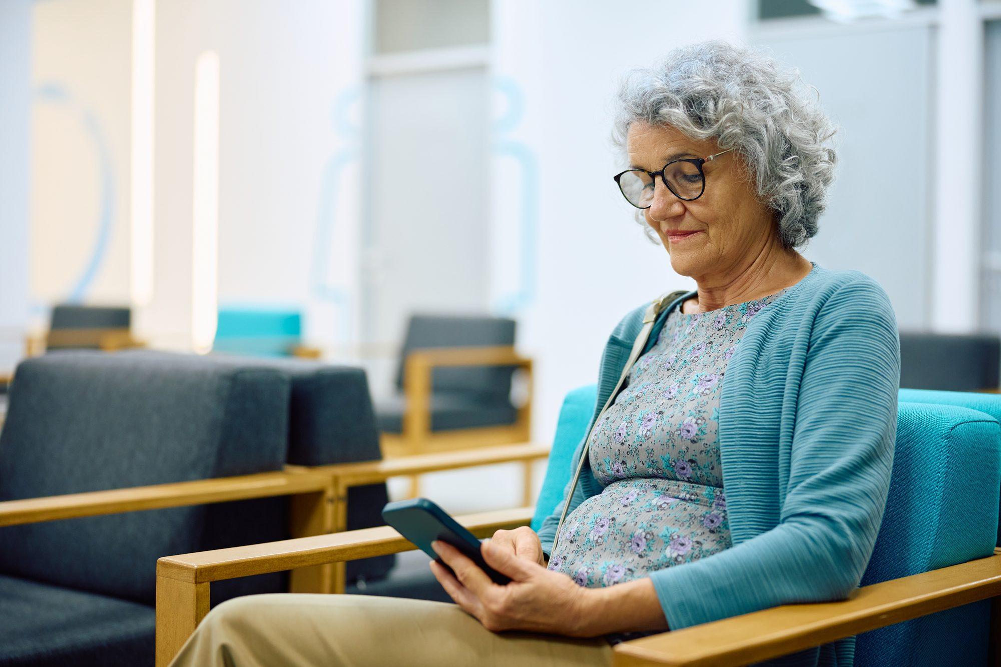 An older woman sitting in a waiting room, checking her phone